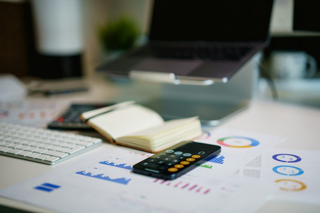 A desk with a laptop, calculator and printed finance charts