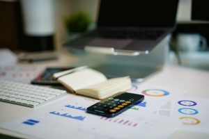 A desk with a laptop, calculator and printed finance charts