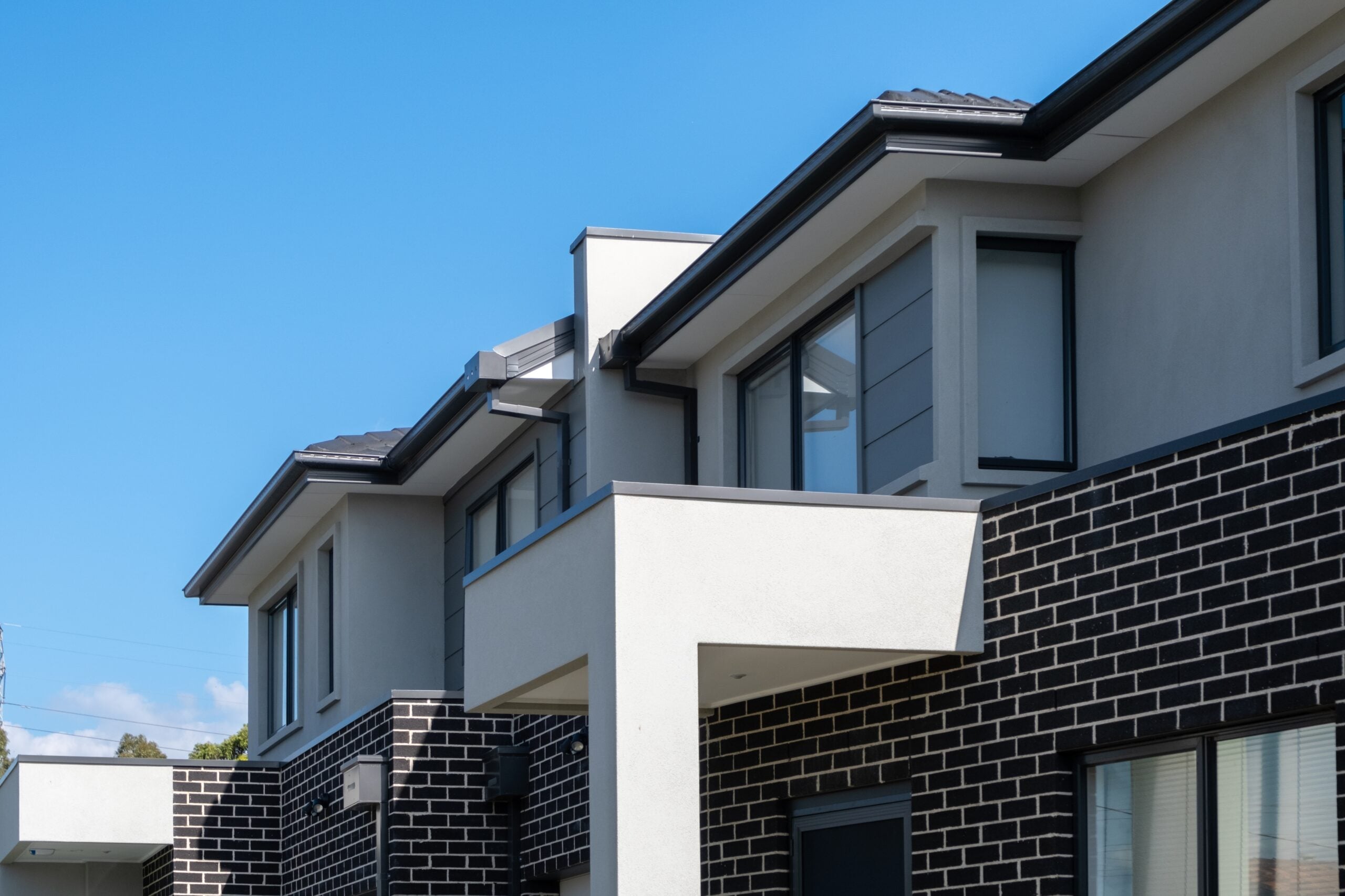 A row of modern two-storey homes in dark brick and light render under a clear sky